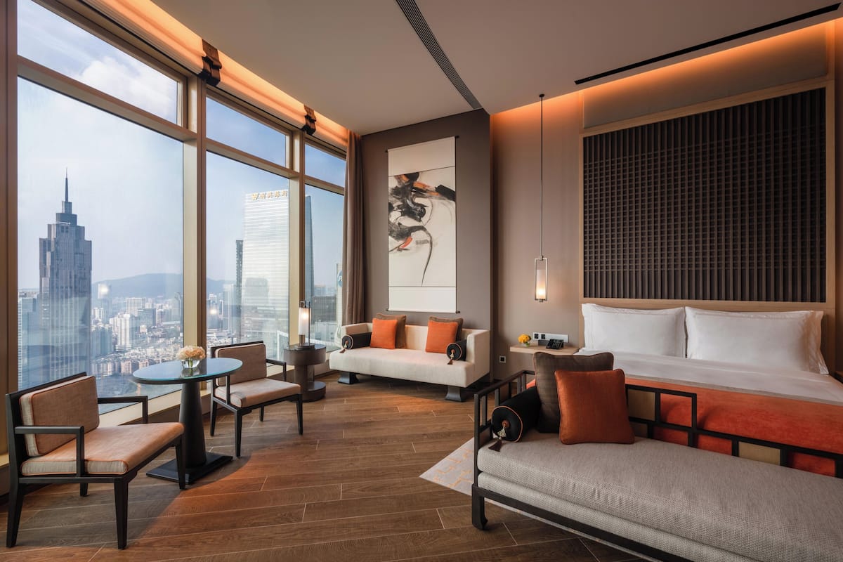 Une chambre d’hôtel moderne avec vue sur la ville, comprenant un canapé, une table à manger et une grande peinture abstraite.