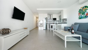 Een moderne woonkamer met een flatscreen televisie, een bank, een salontafel en een keuken op de achtergrond.