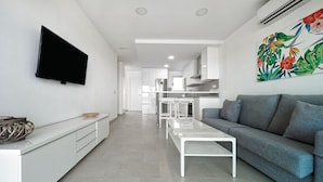 Een moderne woonkamer met een grijze bank, een witte salontafel en een flatscreen televisie die aan de muur is bevestigd.