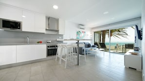 Een moderne keuken met witte kastjes, een magnetron en een groot raam met uitzicht op zee.