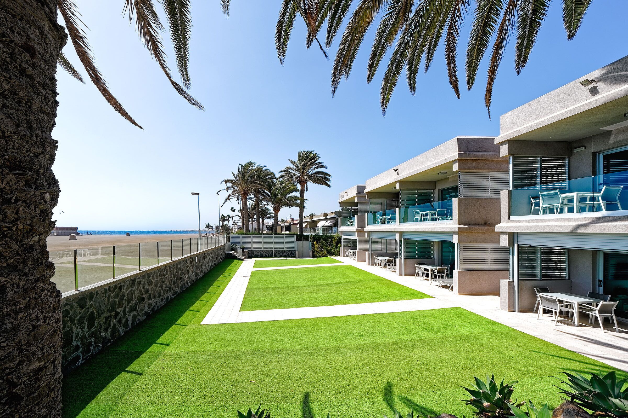 A modern hotel with a well-maintained lawn, outdoor seating, and a view of the beach.