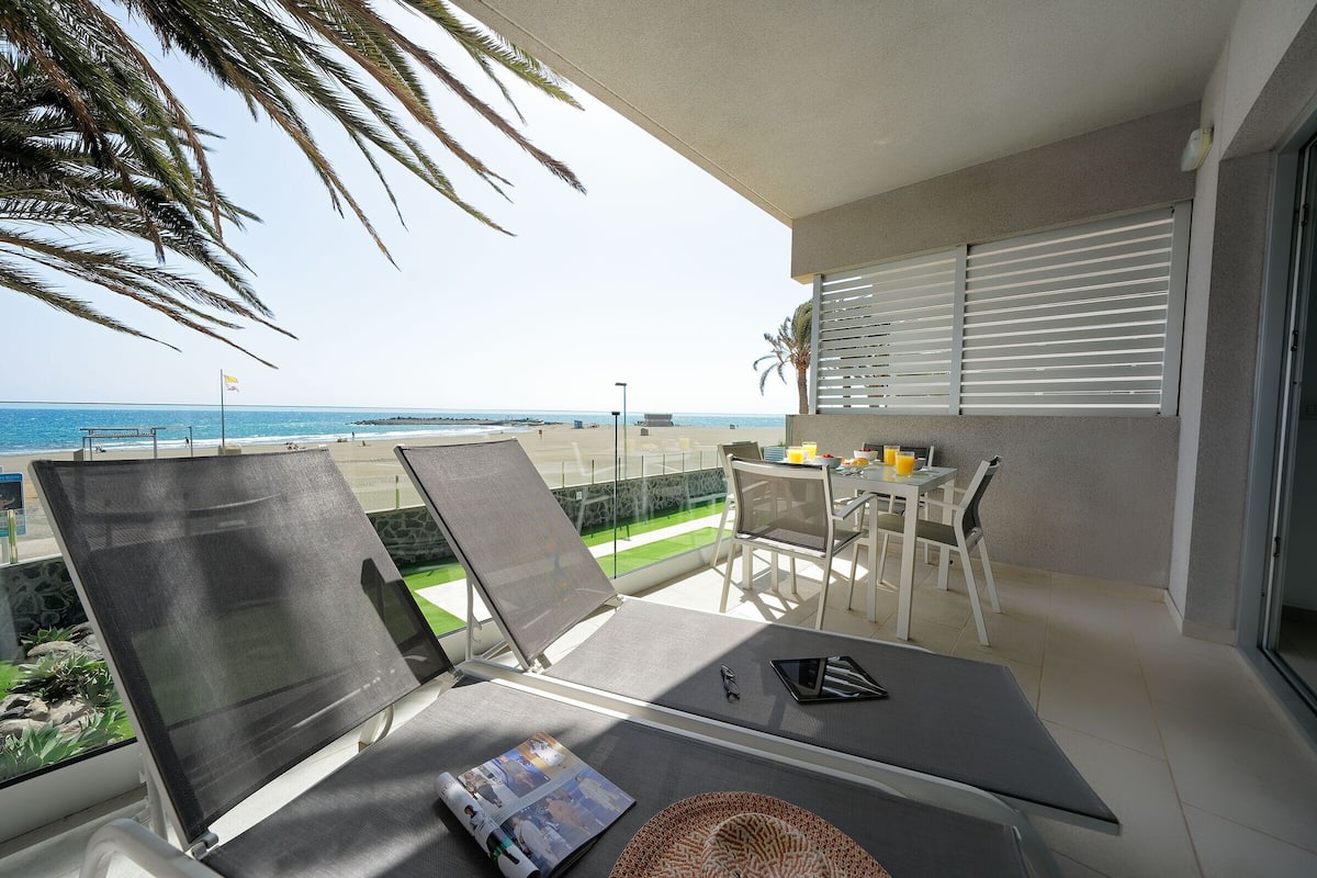 Un balcon avec des chaises longues, une table et des chaises, et une vue sur la plage.