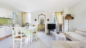 Un salon comprenant un canapé, une table à manger avec des chaises, un téléviseur et un coin cuisine avec des placards et un évier.