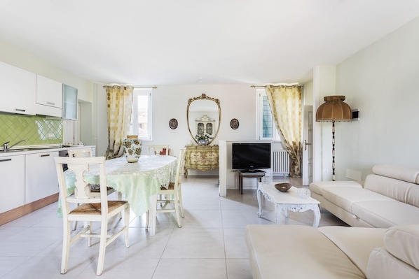 A living room with a sofa, a dining table with chairs, a TV, and a kitchen area with cabinets and a sink.