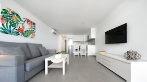 A modern living room with a grey sofa, a white coffee table, and a flat-screen TV mounted on the wall. - Apartamentos Los Papagayos (San Bartolomé de Tirajana)
