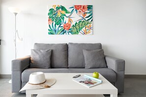 Una sala de estar moderna con un sofá gris, una mesa de centro blanca y una obra de arte de temática tropical y colorida en la pared.