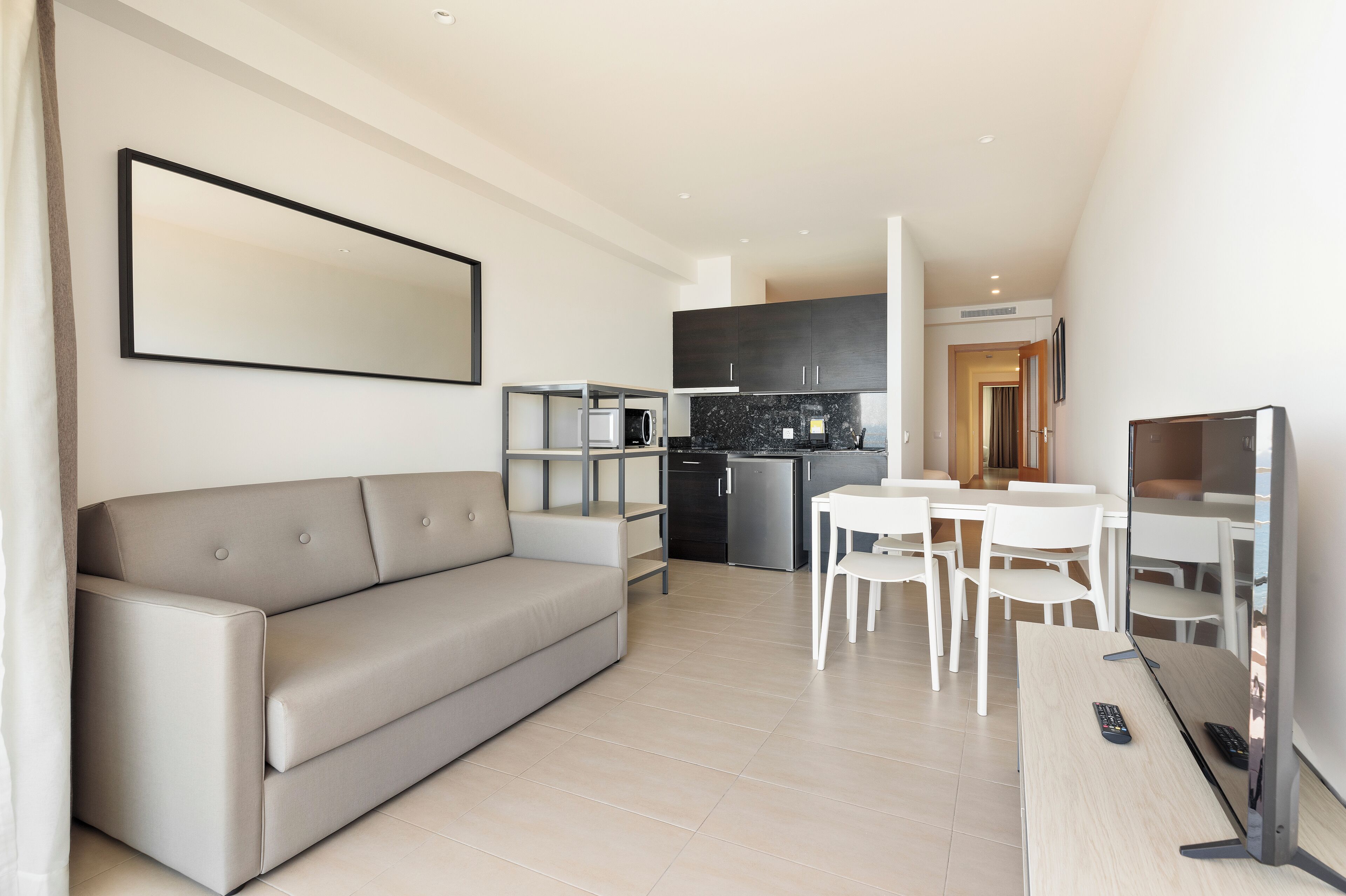 Una sala de estar moderna con un sofá, una mesa de comedor con sillas, un televisor y una cocina al fondo.