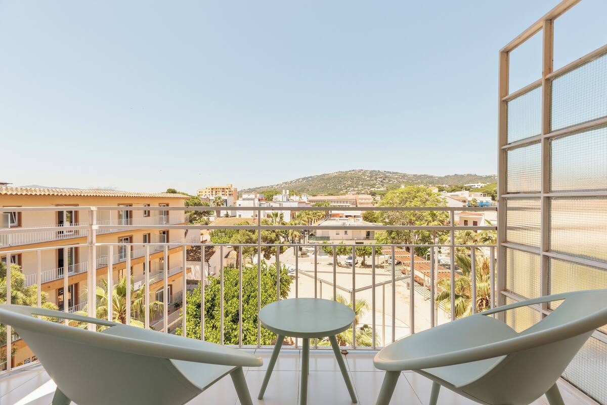 Un balcon avec deux chaises et une petite table, donnant sur un quartier résidentiel avec des immeubles et de la verdure.
