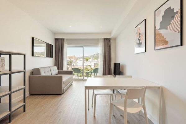 A modern living room with a sofa, a dining table with chairs, a TV, and artwork on the walls.