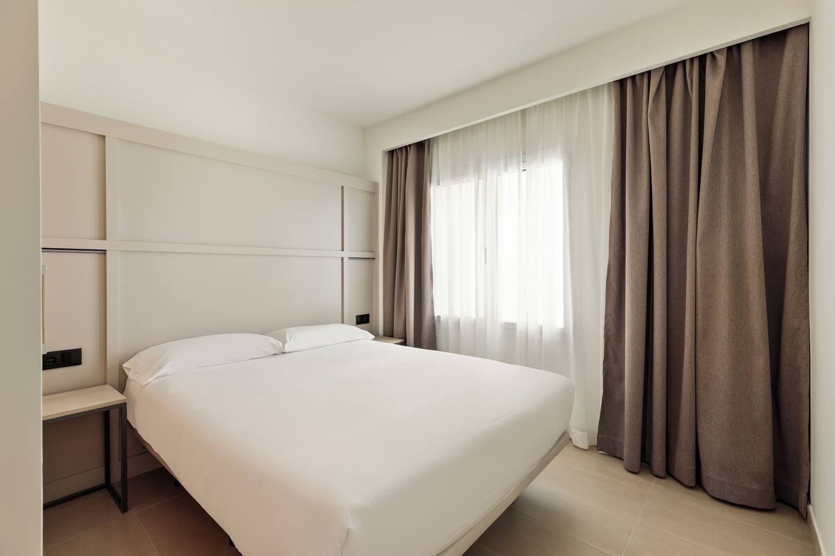 Une chambre d’hôtel moderne avec un grand lit, une table de chevet et une fenêtre avec des rideaux.