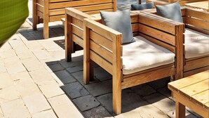 Mobiliario de madera exterior con cojines, un área empedrada de piedra y vistas a la playa y al océano.