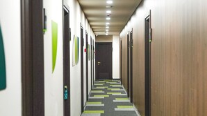 Un pasillo de hotel con alfombra a cuadros, puertas a ambos lados y un techo con iluminación empotrada.