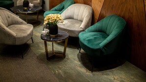 Un área de descanso moderna con un panel de madera geométrico, un reloj y dos sillones verdes.