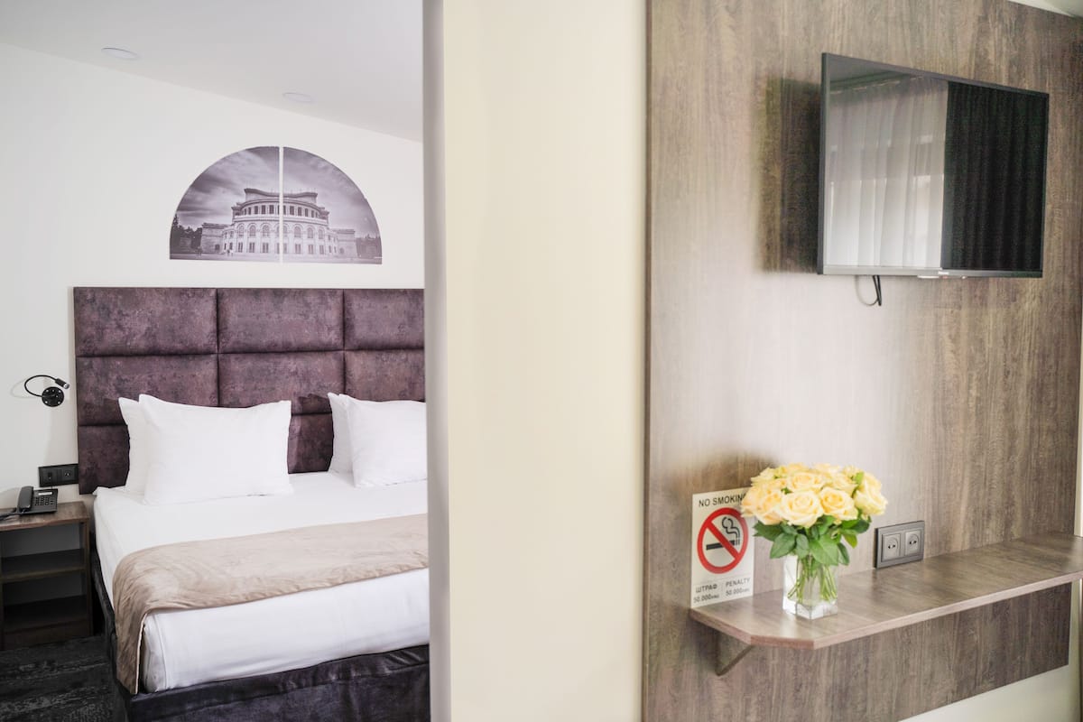 A hotel room with a large bed, a mounted TV, a no-smoking sign, and a framed picture on the wall.