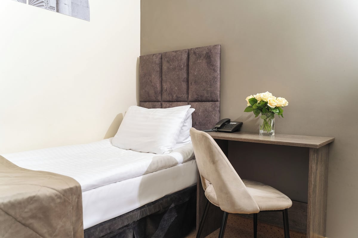 A hotel room with a bed, a chair, a desk with a telephone, and a vase with flowers.