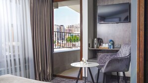 Una habitación de hotel con una cama, una mesita redonda con una silla, un televisor montado en la pared y un balcón con vistas a la ciudad.