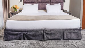 Una cama grande con cabecera, dos mesitas de noche, un jarrón con flores y un cuadro colgado en la pared.