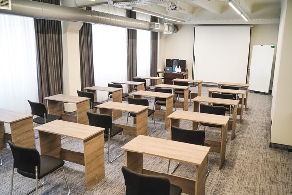 A classroom with desks and chairs arranged in rows, a projector screen, and a whiteboard.