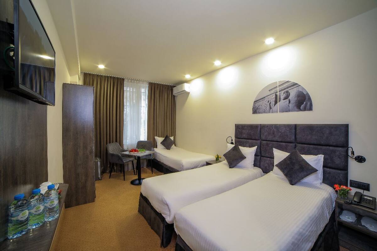 A hotel room with two beds, a desk, a chair, a TV, and a water dispenser.