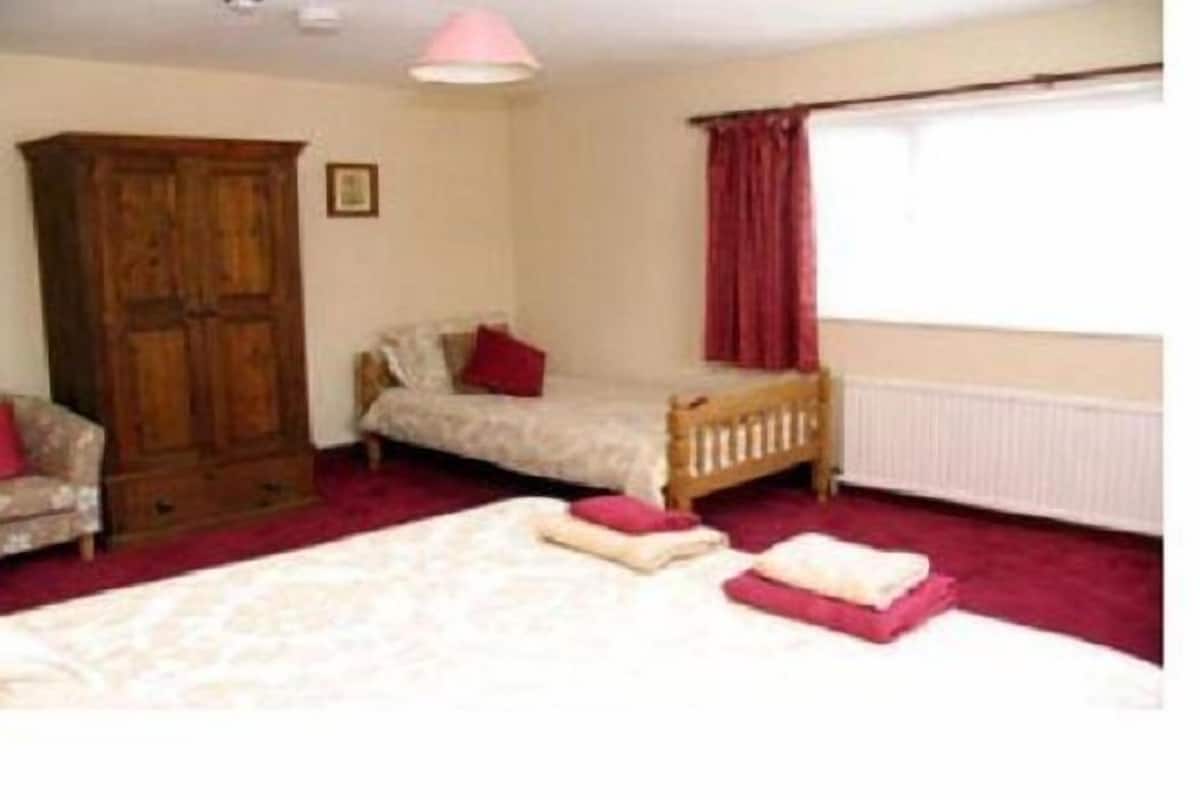 Quarto com uma cama, um guarda-roupa de madeira, um sofá pequeno e uma janela com cortinas.