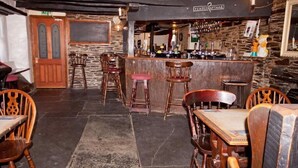 Zona de bar con sillas y mesas de madera, pared de piedra y mostrador con grifos.