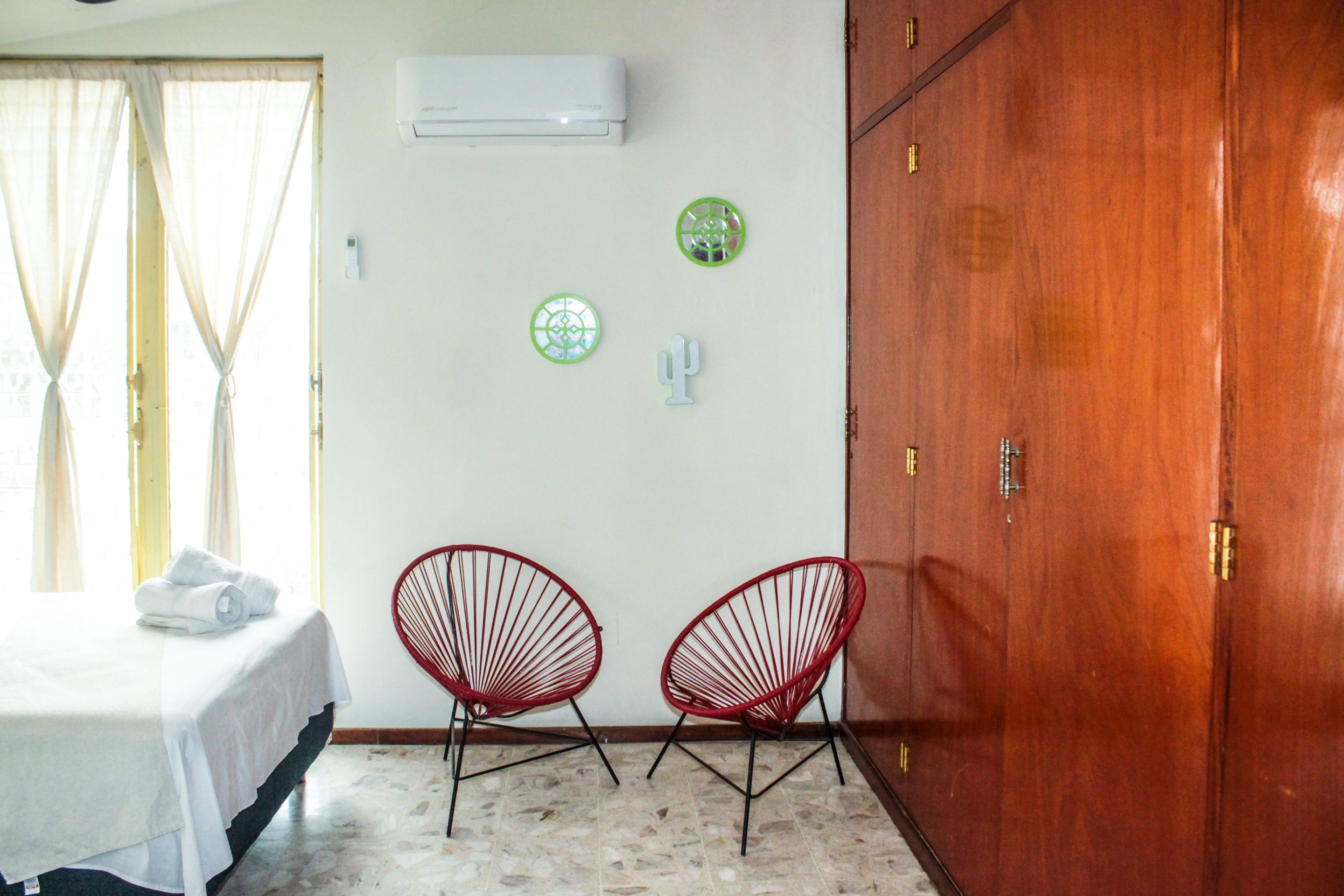 Quarto com uma cama, duas cadeiras vermelhas, um guarda-roupa e pratos decorativos na parede.