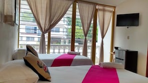A hotel room with two beds, a television, and a balcony with curtains. - Villa Mandarina Suites Tuxpan (Tuxpan)