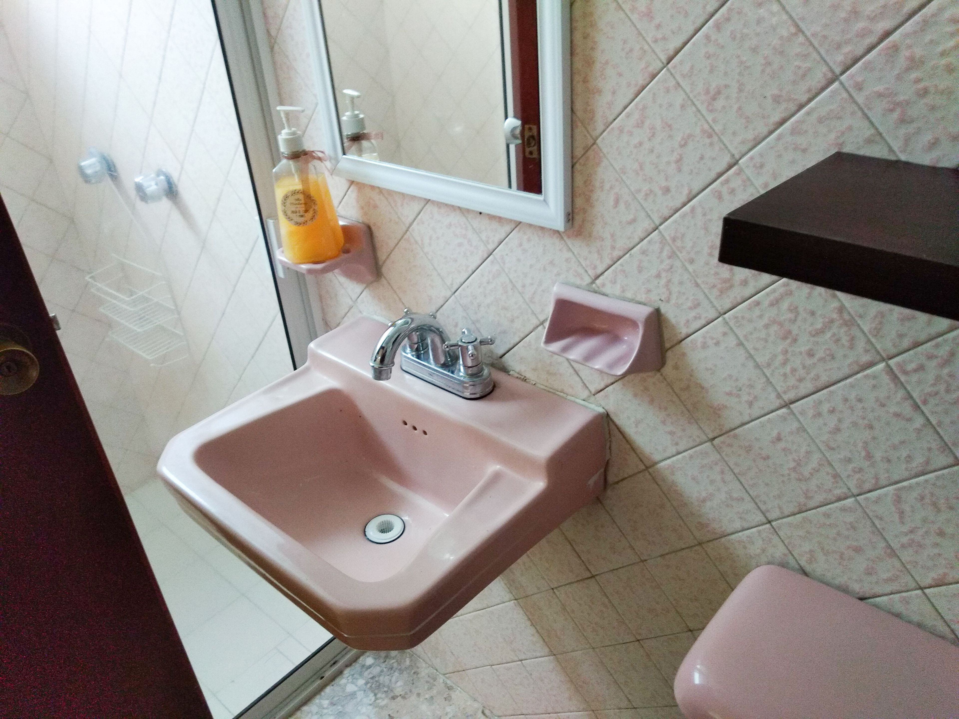 A bathroom with a pink sink, a mirror, and a toilet.