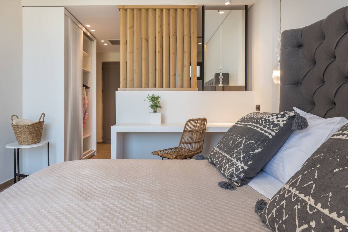 Ein Schlafzimmer mit einem großen Bett, einem Sessel, einem kleinen Tisch, einem Korb, einer Pflanze und einem Spiegel.