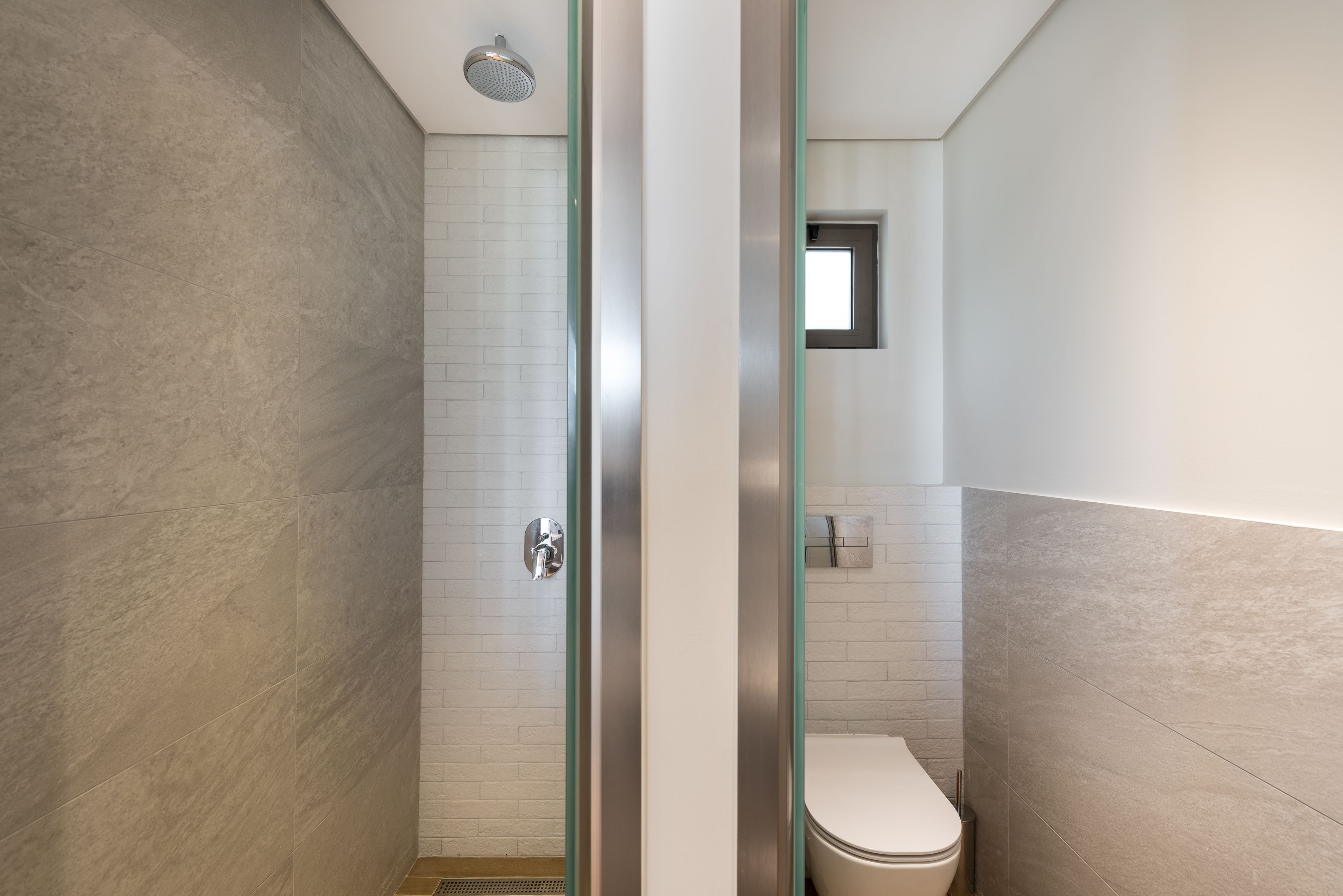A modern bathroom with a glass shower enclosure, a white toilet, and a small window.
