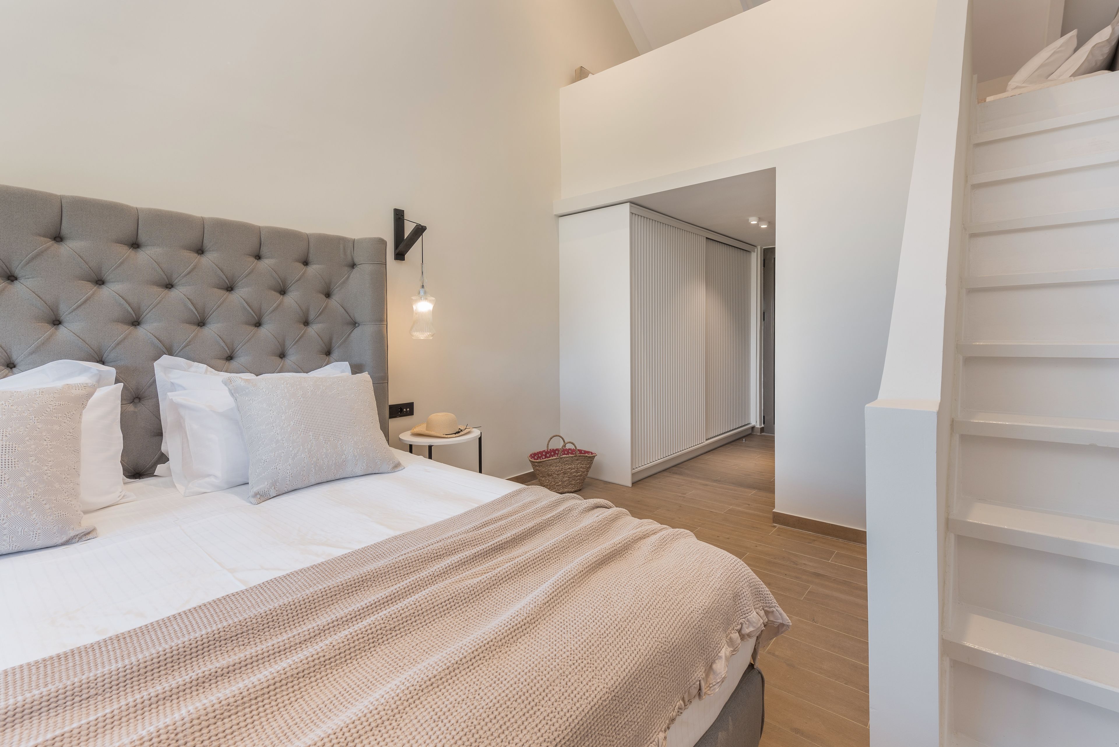 Una camera da letto con una testiera trapuntata, un letto grande con lenzuola bianche, un comodino con una lampada e vista su una porta scorrevole che dà su un'altra stanza.