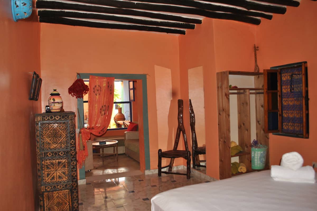 A room with a bed, a wooden chair, a small table, and a decorative cabinet.