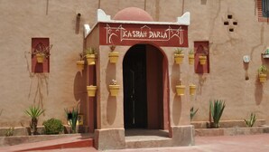 A building entrance with a sign reading "Kasbah Darla" and multiple potted plants around the entrance. - Auberge Kasbah Darla (Aghouatim)