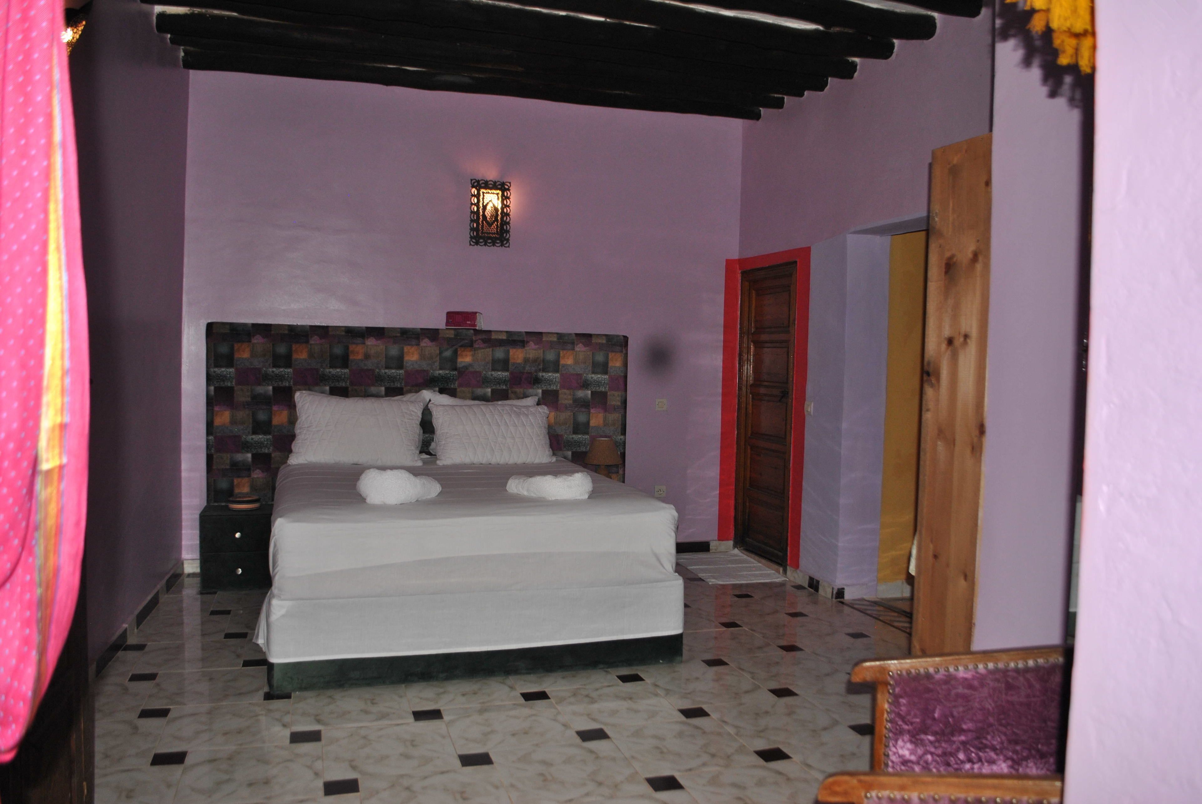 Un dormitorio con una cama grande, una mesita de noche, una lámpara de pared y una puerta.