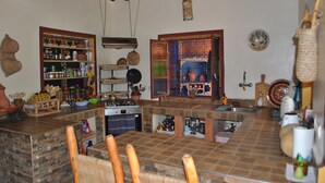 A kitchen with a central island, wooden chairs, and a hanging light fixture. - Auberge Kasbah Darla (Aghouatim)