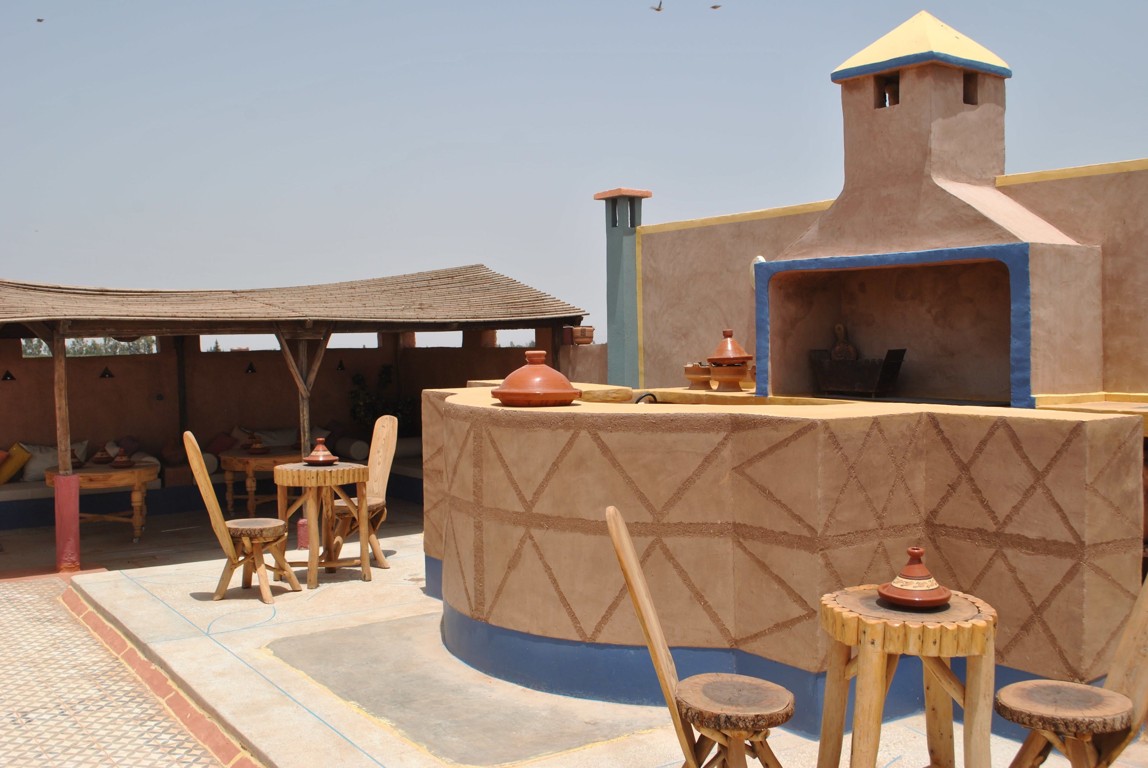 An outdoor seating area with wooden furniture and a central round table, surrounded by a low wall with a decorative pattern.