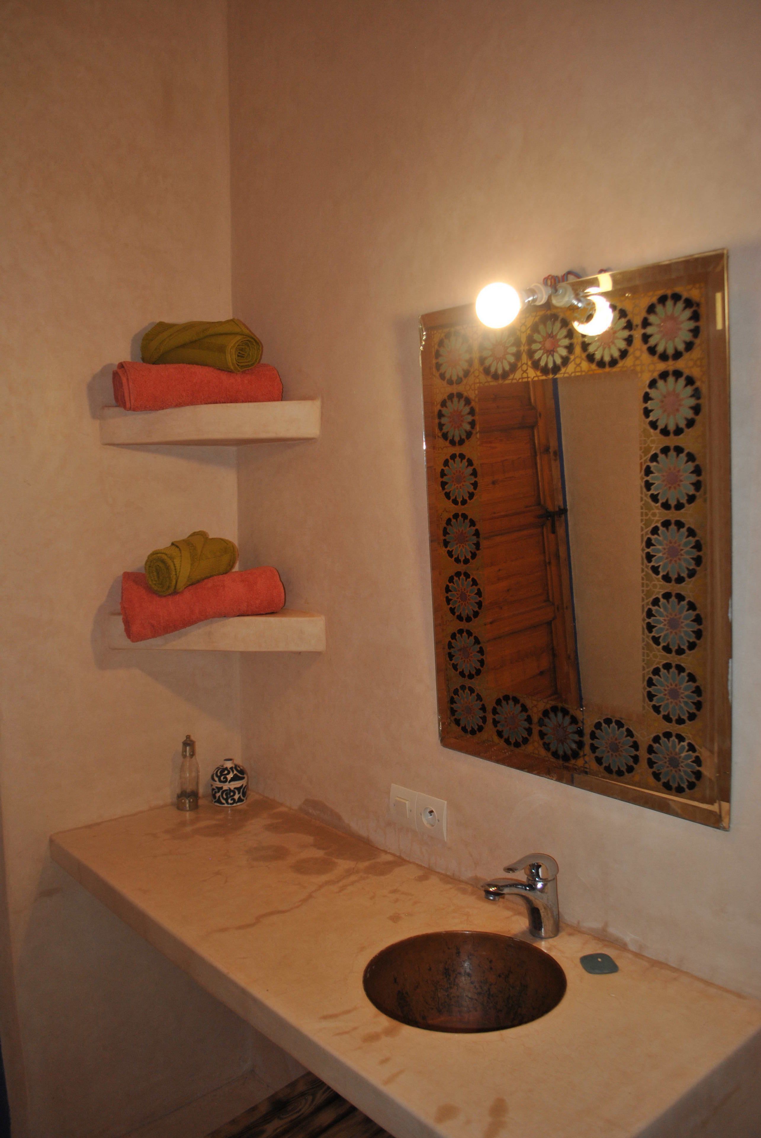 Un baño con un lavabo de madera, un espejo con marco decorativo y dos repisas con toallas enrolladas.
