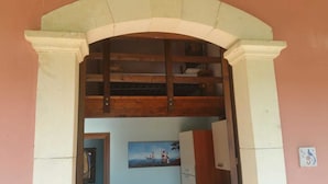 An arched doorway leading to a room with a painting on the wall and a wooden shelf above. - Agriturismo Vita e Natura (Noto)
