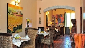 A dining area with wicker furniture, a painting of sunflowers, and a statue. - Agriturismo Vita e Natura (Noto)