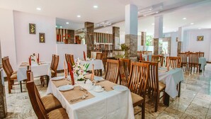 Un restaurante con varias mesas dispuestas para comer, sillas de madera y piso de baldosas.