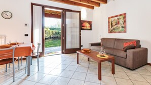 Un salon comprenant un canapé, une table à manger avec des chaises, une table basse, un tableau, une horloge et une porte-fenêtre coulissante donnant sur un jardin.