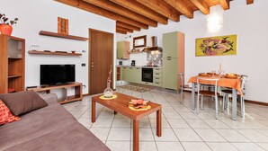 Un salon moderne comprenant un canapé, un téléviseur, une table basse en bois et un coin repas avec une table dressée pour quatre personnes.