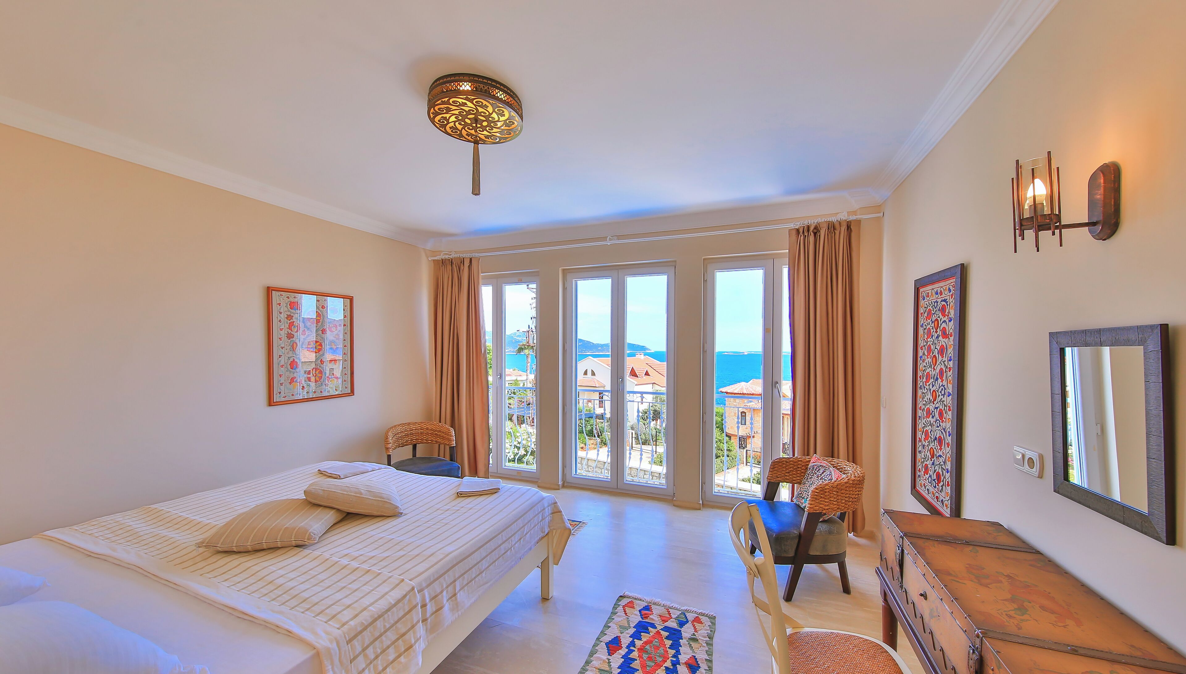 A bedroom with a bed, a chair, a dresser, and a view of the sea through large windows.