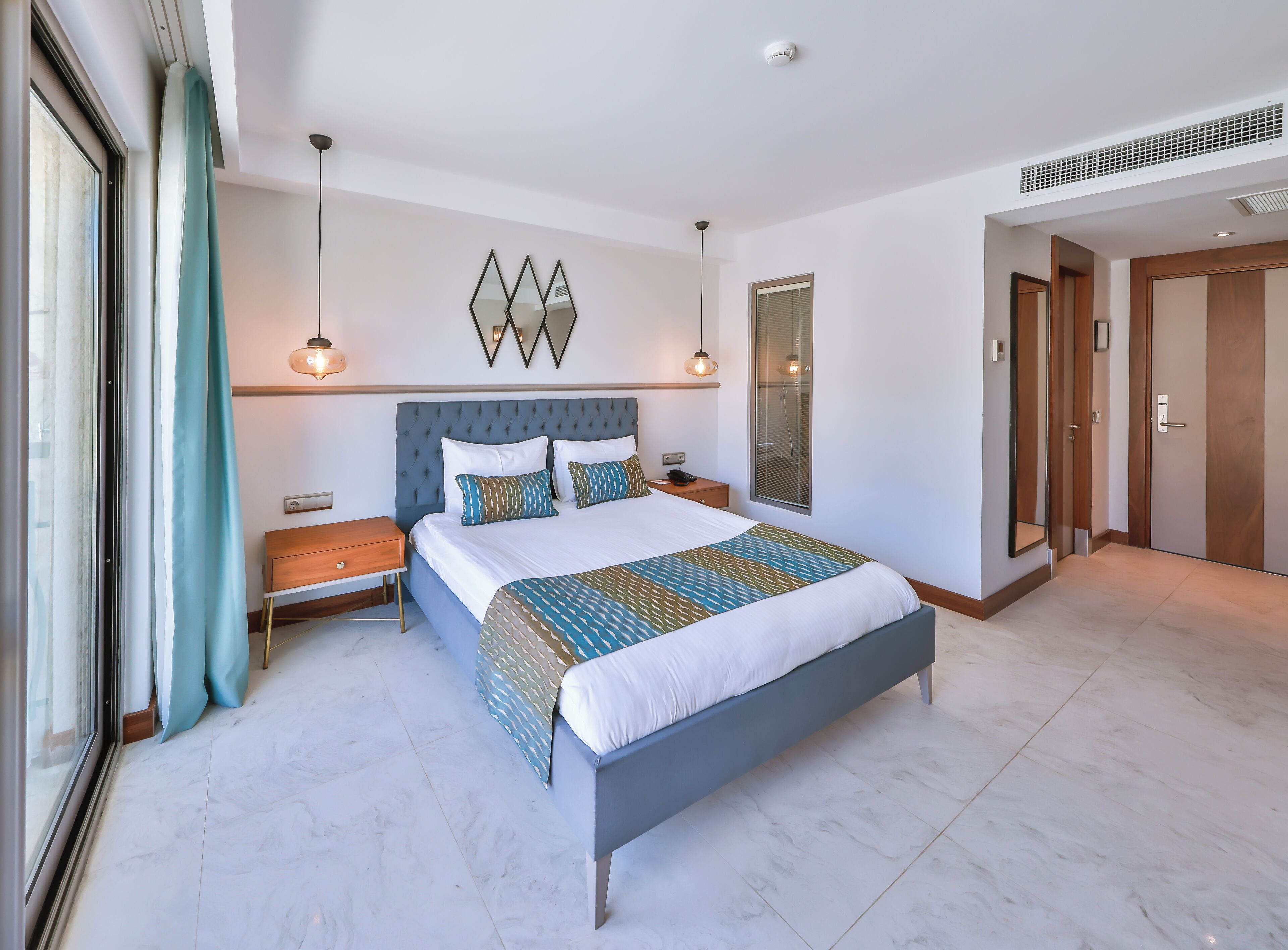 A modern hotel room with a large bed, bedside tables, a wardrobe, and a bathroom with a shower.