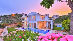 A modern two-story house with a swimming pool, surrounded by lush greenery and flowering plants. - Molino Hotel (Kas)