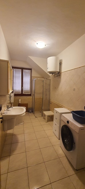 Een kleine badkamer met een wastafel, toilet, douche en wasmachine.