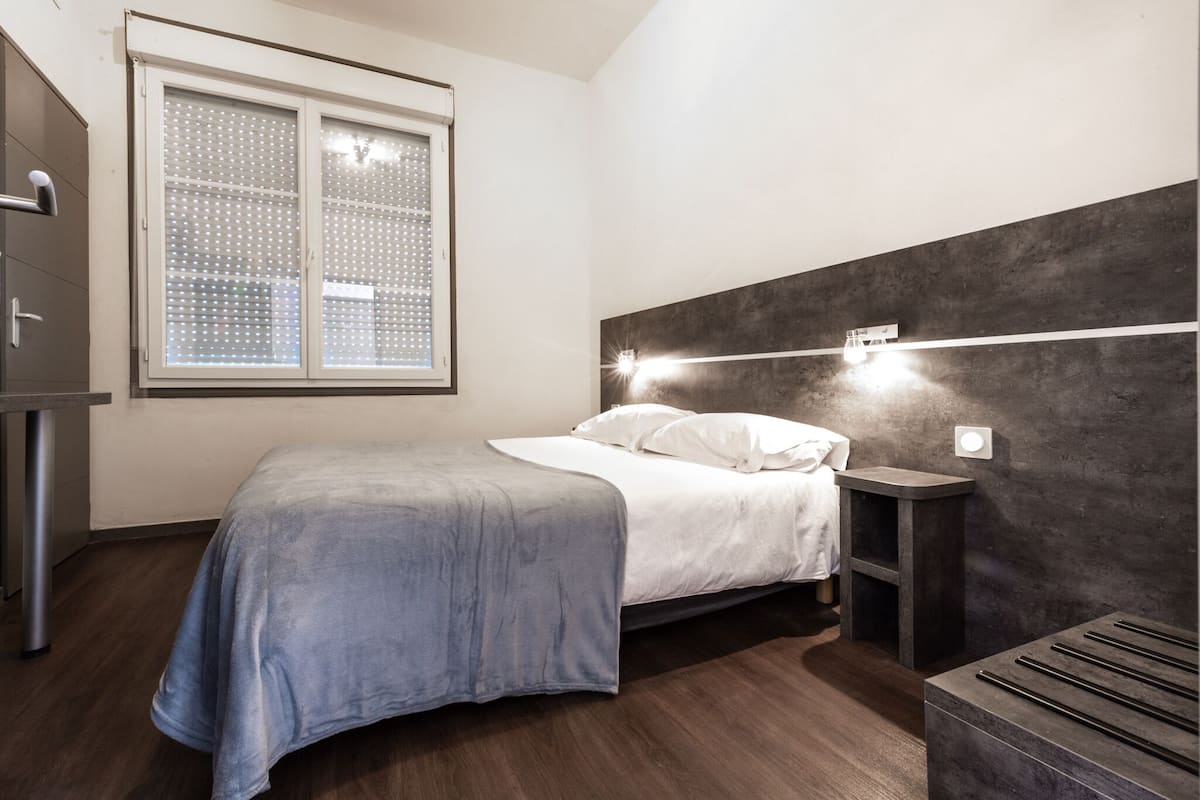 A modern bedroom with a bed, bedside table, and a window with blinds.