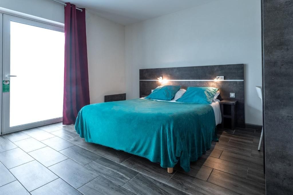 A bedroom with a bed, a nightstand, a wall-mounted light, and a sliding glass door.
