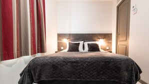 Een net opgemaakt bed met een donker beddegoed, twee bedlampjes en een hoofdbord.