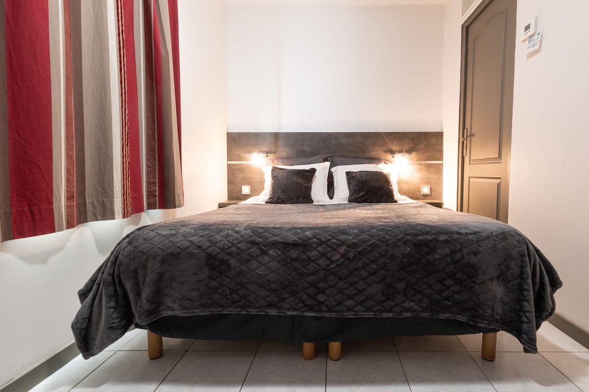 A neatly made bed with a dark patterned bedspread, two bedside lamps, and a headboard.